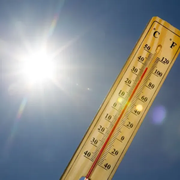 Thermometer being held up next to blue sky and sun.